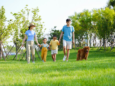 Happy family of four walking with the pet dog in the park