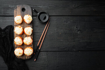 Baked sushi maki rolls with salmon, crab, cucumber, avocado, flying fish roe and spicy sauce, on black wooden table background, top view flat lay , with copyspace  and space for text