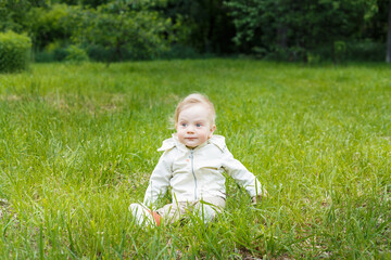 Portrait of a little white caucasian boy. On a summer day, a child sits on the grass in a park.