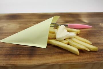 Pommes Frites in einer Tüte mit Mayonnaise und Piekser auf einem Holzbrett