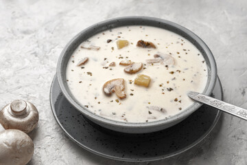 Soup with mushrooms and coconut cream in a gray plate next to raw mushrooms.