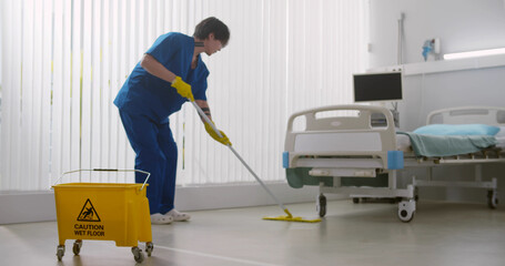 Asian male nurse washing floor with mop in empty hospital ward