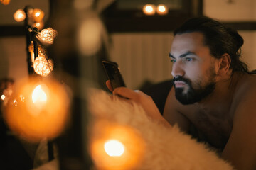 Young man with phone in bed in the evening. Evening leisure at home