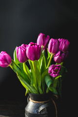 Lilac purple tulip flowers on table. Spring bouquet flowers in vintage vase. Floral concept. Floral background. Dark black background.