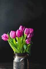 Lilac purple tulip flowers on table. Spring bouquet flowers in vintage vase. Floral concept. Floral background. Dark black background.