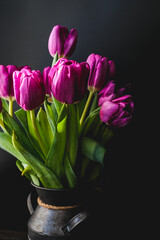 Lilac purple tulip flowers on table. Spring bouquet flowers in vintage vase. Floral concept. Floral background. Dark black background.