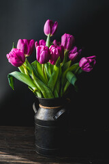 Lilac purple tulip flowers on table. Spring bouquet flowers in vintage vase. Floral concept. Floral background. Dark black background.