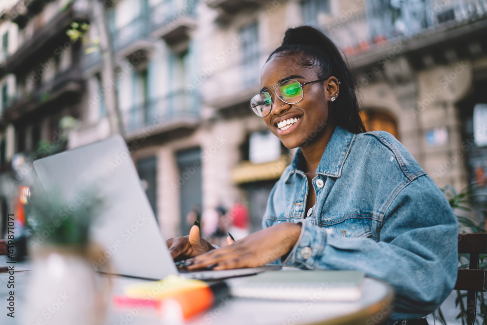 Aufkleber smiling dark skinned female blogger typing text while messaging using laptop computer working remote
