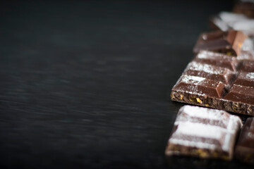 Pieces of chocolate in powdered sugar on a black background.
