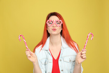 Young woman with bright dyed hair holding candy canes on yellow background