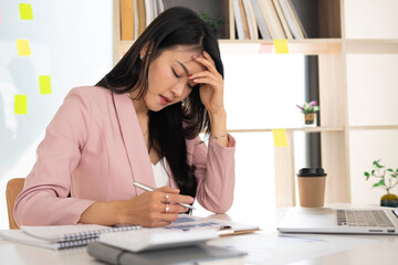 Asian female finance is stressful at work after the company's sales summary has disappeared. A beautiful money manager in a pink suit is stressed out in the office.