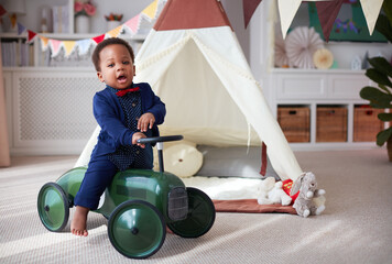 cute one year old baby boy having fun on a push car in a nursery room at home