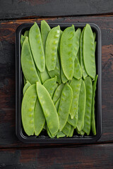 Organic Green Sugar Snap Peas Ready to Eat, in plastic container, on old dark  wooden table background, top view flat lay