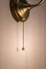 Pulling chain switch of an antique electric wall lamp, close-up part . Interior deocation object...
