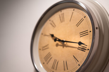 A classic round clock with roman numbers which is installed on white plain wall. Interior decoration object photo.