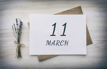 march 11. 11th day of the month, calendar date. White blank of paper with a brown envelope, dry bouquet of lavender flowers on a wooden background. Spring month, day of the year concept