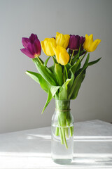 Lilac purple tulip flowers on table. Spring bouquet flowers in vintage vase. Floral concept. Floral background.  White decoration and light background