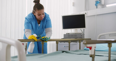 Afro-american nurse cleaning hospital bed with detergent