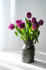 Lilac purple tulip flowers on table. Spring bouquet flowers in vintage vase. Floral concept. Floral background.  White decoration and light background