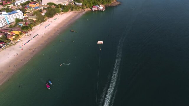 Parasailing on Langkawi island in Malaysia. Active leisure, extreme sports concept. Sandy beach on sunny day with azure sea. Travel, vacation concept. Aerial view, drone shot