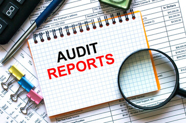 Obraz premium The notebook with the text Audit Reports lies on the financial tables with a calculator a magnifying glass