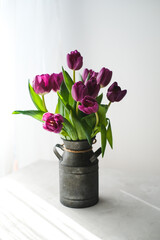 Lilac purple tulip flowers on table. Spring bouquet flowers in vintage vase. Floral concept. Floral background.  White decoration and light background