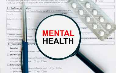 Magnifying glass with text Mental Health inside lies on medical documents with pills and a blue metal pen