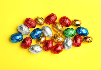 Fototapeta na wymiar Chocolate eggs wrapped in colorful foil on yellow background, flat lay