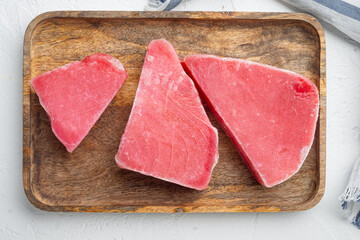 Obraz na płótnie Canvas Frozen tuna fish steaks, on wooden tray, on white stone background, top view flat lay