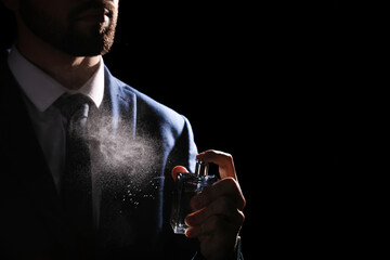 Man spraying luxury perfume on black background, closeup - obrazy, fototapety, plakaty