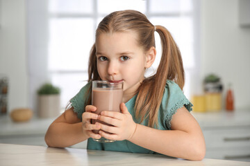 Cute little child drinking tasty chocolate milk in kitchen