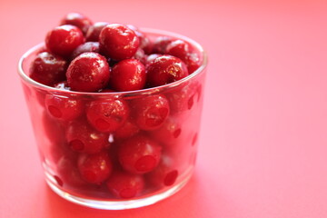 cherry in a glass on a pink red background with a place to text the view from the side close-up of the copyspace