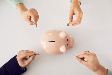 Hands putting money in pink piggy bank on white table background. People saving up together, family...