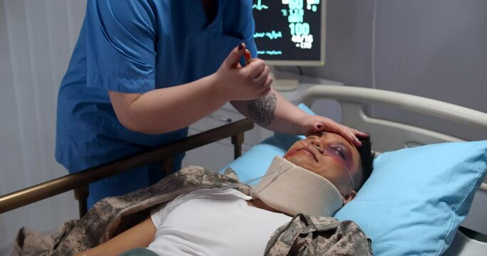 Doctor checking condition of unconscious injured soldier in hospital ward