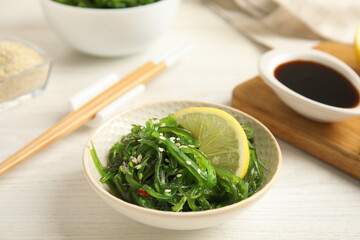 Japanese seaweed salad with lemon slice served on white wooden table, closeup