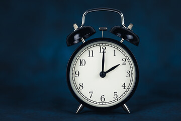 Black vintage alarm clock shows 2 o'clock isolated on dark background.