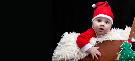 Funny Christmas child in a Santa Claus hat in a retro suitcase on a black background. Kid in Christmas.