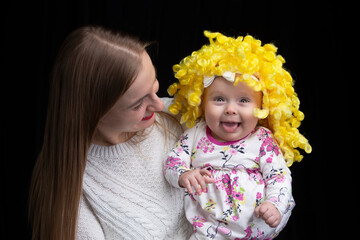 Mom holds in her arms a little happy daughter in a yellow wig. Funny kids.