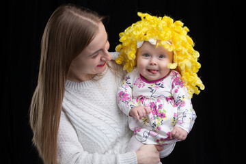 Mom holds in her arms a little happy daughter in a yellow wig. Funny kids.