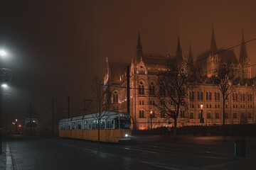 Fototapeta na wymiar Tram line near the Hungarian Parliament. The old yellow tram in Budapest. Night foggy view. 