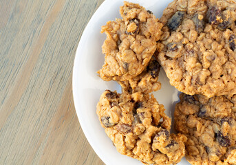 Top close view of a white plate with homemade oatmeal raisin cookies with one broken illuminated with natural light.