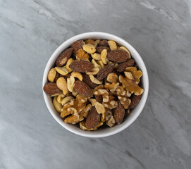 Top view of assorted nuts in a white bowl on a fake gray marble tile.
