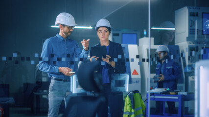 Modern Factory: Female Project Manager, Male Engineer Standing in High Tech Development Facility, Talking and Using Tablet Computer. Contemporary Facility with CNC Machinery, Robot Arm Production Line