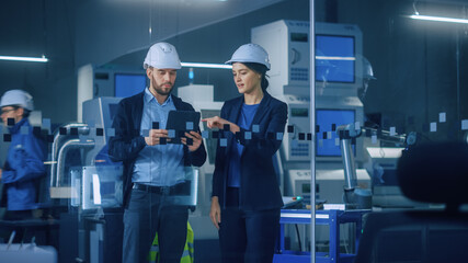 Modern Factory: Female Project Manager, Male Engineer Standing in High Tech Development Facility, Talking and Using Tablet Computer. Contemporary Facility with CNC Machinery, Robot Arm Production Line