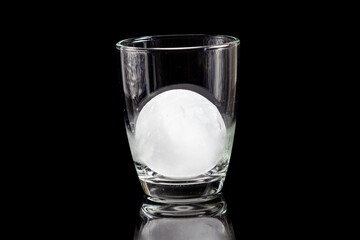 ice ball inside cocktail glass on a reflective black table.