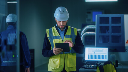 Professional Engineer Wearing Safety Vest and Hardhat Walks Through Modern Factory Workshop, Uses...