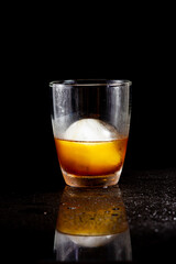 Cold americano decoration with ice ball in whisky glass on a black table.