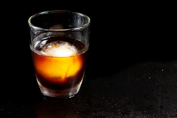 Cold americano decoration with ice ball in whisky glass on a black table.
