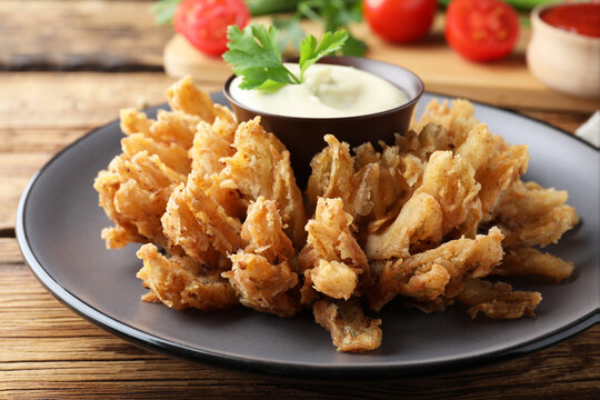 Fried blooming onion with dipping sauce served on wooden table, closeup