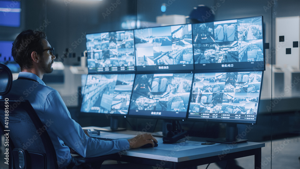 Poster Industry 4.0 Modern Factory: Security Operator Controls Proper Functioning of Workshop Production Line, Uses Computer with Screens Showing Surveillance Camera Feed. High-Tech Security